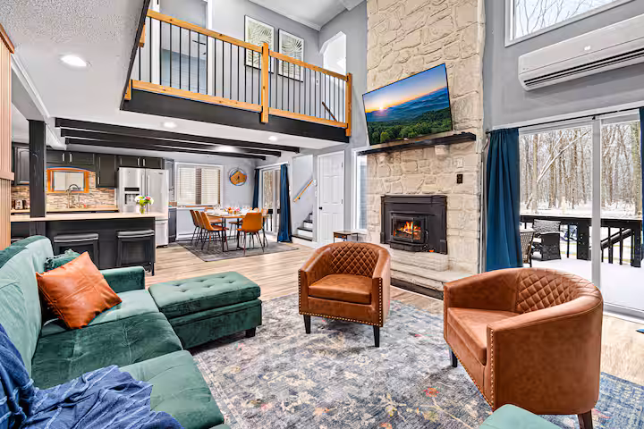 Great room with stone fireplace, floor-to-ceiling windows, and snowy woodland view